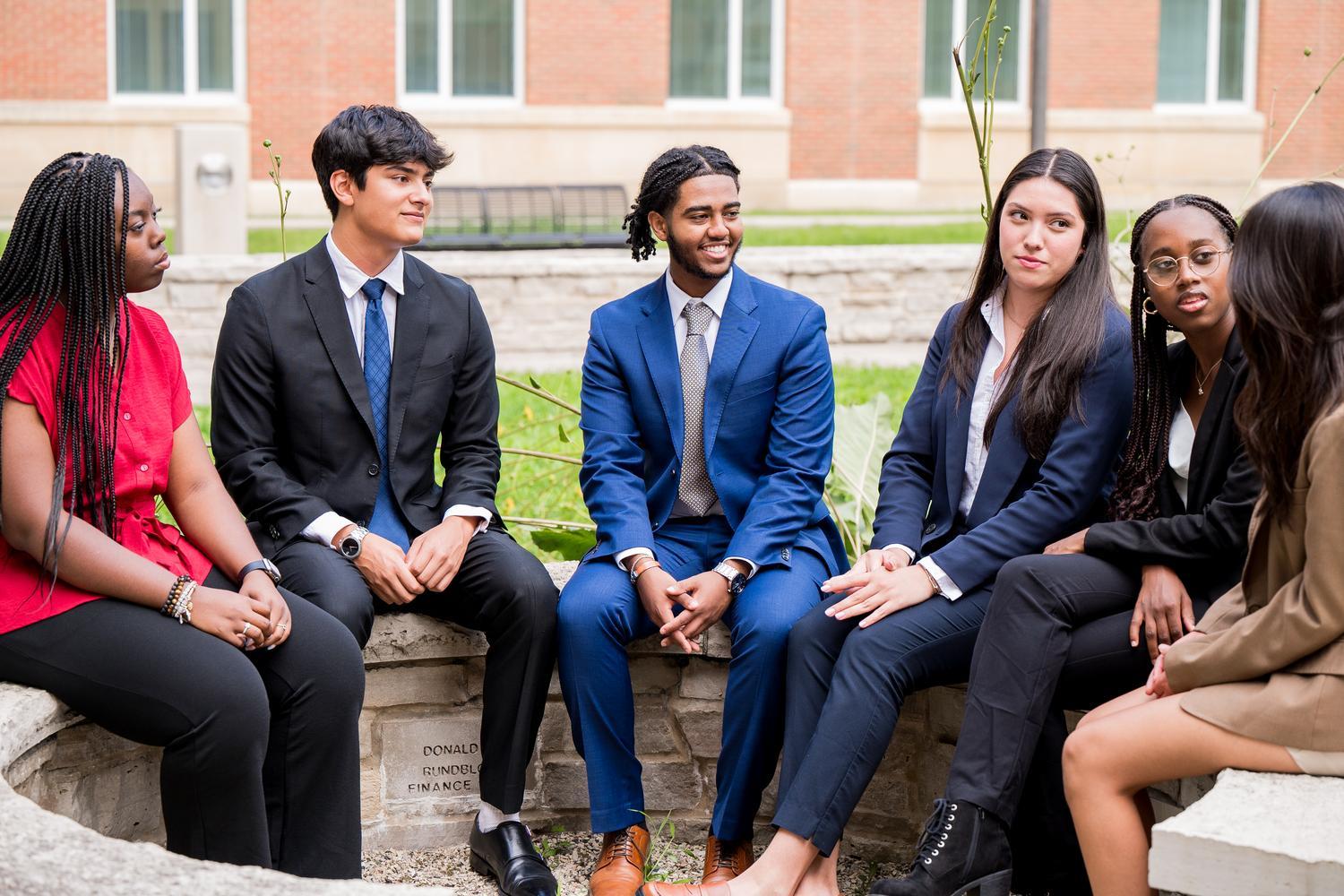 Students in suits gathered outside sitting in discussion.