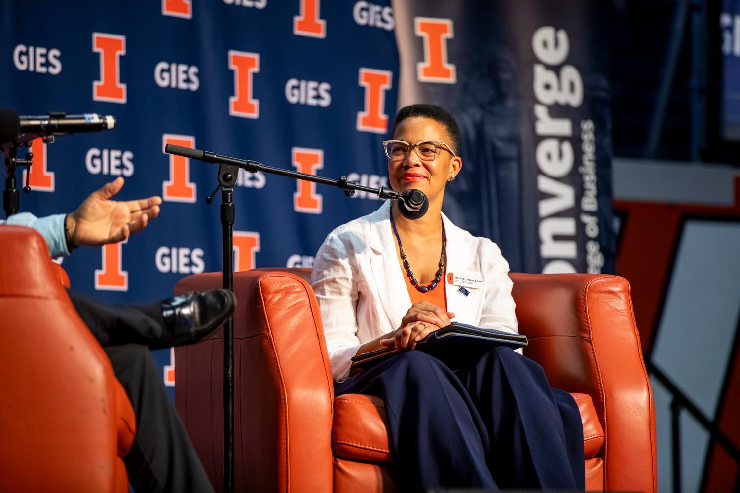 Woman speaking on panel in orange chair with microphone in front of her