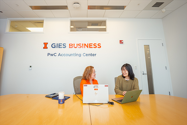 Staff and Student Talking at Table in front of PwC Accounting Center and Gies Business Sign Staff and Student Talking at Table in front of PwC Accounting Center and Gies Business Sign