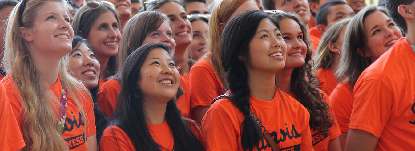 University students in orange tshirts looking up at speaker