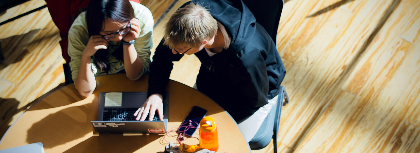 Two students leaning over a computer at a table