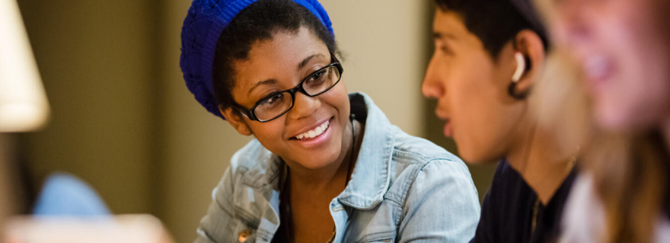 Female university student with blue hat and glasses talking with fellow classmates