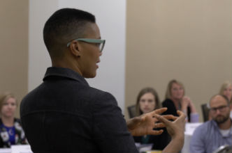 Company Reputation Instructor speaks in front of a group of students in classroom setting.