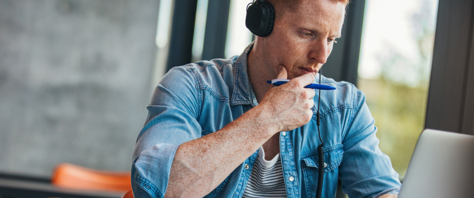 CTA Image for PMBA Male student with headphones in blue shirt working at a laptop computer
